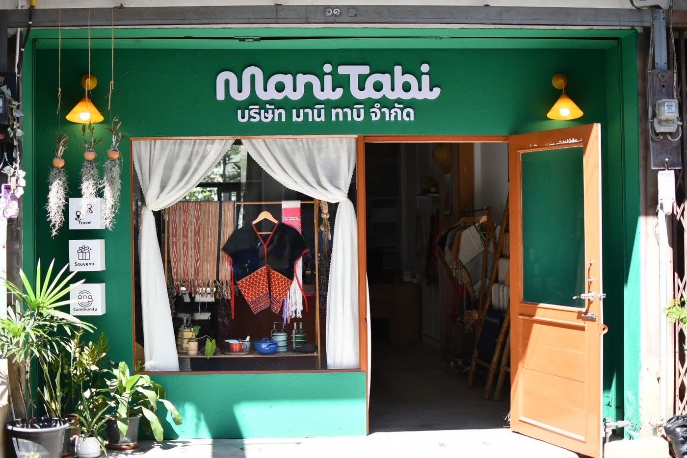 チェンマイ市内にあるマニタビショップの外観。緑の壁にMani Tabiの看板、店先に手織りの布や民族衣装が並ぶ